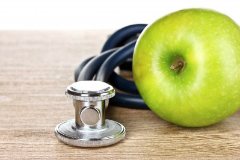 Photo of an apple on a table with a stethoscope next to it
