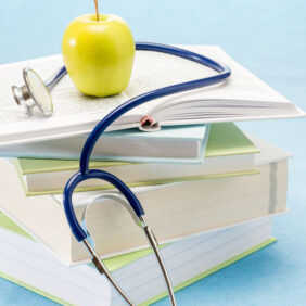 Photo of books stacked with a yellow apple on top and a stethoscope around the Apple