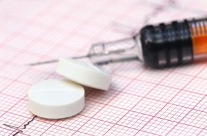 Photograph of pills with syringe in the background representing unsuccessful migraine headache treatment and offering ways to Avoid Becoming a Statistic in the Opioid Epidemic