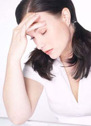 Women with white dress and dark hair with elbow resting on a clear glass table is holding her painful head