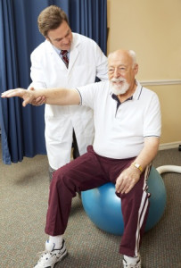 Doctor in white lab coat conducting an older gentleman in exercise ball therapy