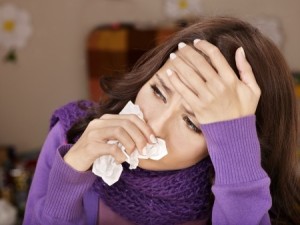 Woman suffering from allergies wipping nose with tissue and holding her head