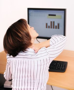 Photograph of a woman working at a computer holding her neck and shoulder